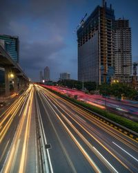 Light trails on road by buildings in city against sky