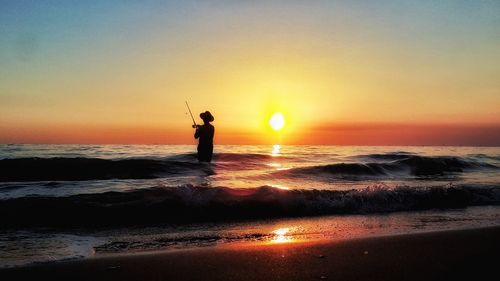 Silhouette man standing on beach against sky during sunset