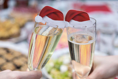 Cropped hands of friends toasting champagne flutes with santa hats at table