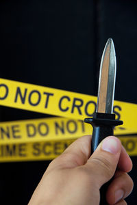 Close-up of hand holding knife against cordon tape