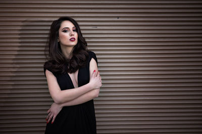 Portrait of beautiful young woman standing against shutter