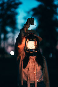 Woman photographing illuminated lamp at night