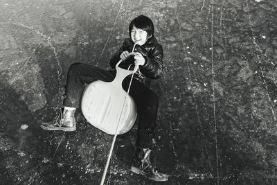 High angle portrait of smiling girl with metal holding rope while sitting on land