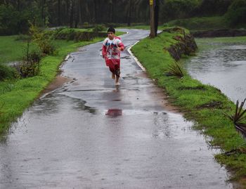 Full length of boy on wet road by tree during rainy season