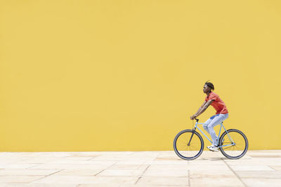 Black guy riding bicycle near wall