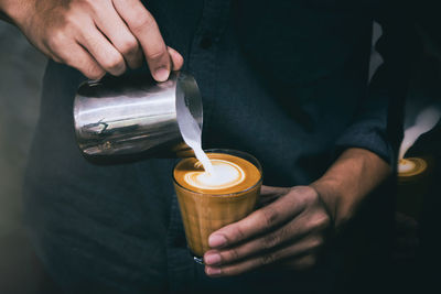 Midsection of man pouring milk in coffee cup