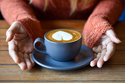 Cropped hand of woman holding coffee on table