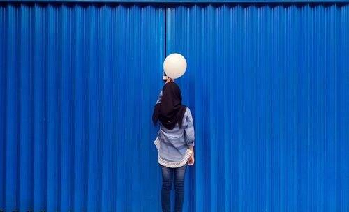 Rear view of person wearing hat standing against blue wall