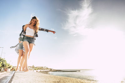 Full length of friends walking on retaining wall at beach against sky