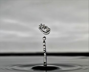 Close-up of drop falling on water against sky
