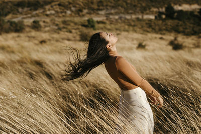 Carefree woman standing amidst grass in field during windy day
