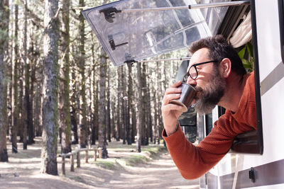 Young man drinking water against trees