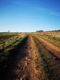 Dirt road amidst field against clear sky