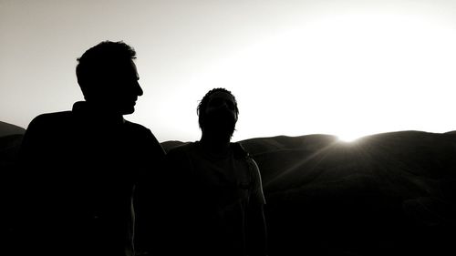 Silhouette friends standing on mountain against sky during sunset