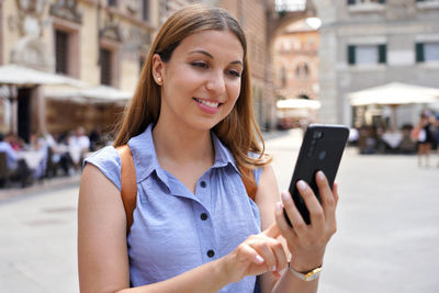 Portrait of smiling woman using mobile phone in city