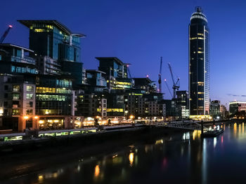 Illuminated buildings by river against sky at night