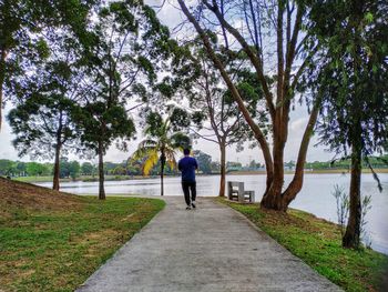 Rear view of man walking on footpath against lake