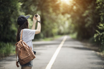 Woman photographing while standing on road against trees