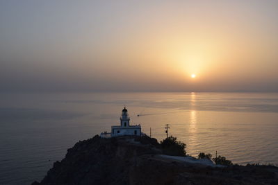 Lighthouse by sea against sky during sunset