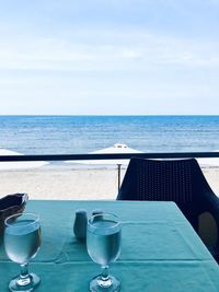 Glass of table by swimming pool against sky