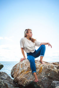 Young woman standing on rock at sea shore against sky