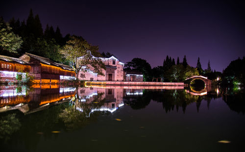 Illuminated buildings by lake against sky at night