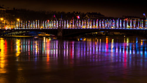 Illuminated bridge over river in city at night