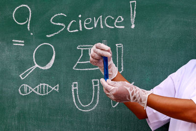 Midsection of scientist examining test tube by blackboard