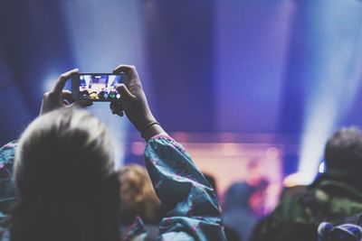 Rear view of woman photographing through smart phone at concert