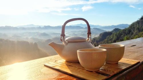 Close-up of cups and teapot on table against mountains