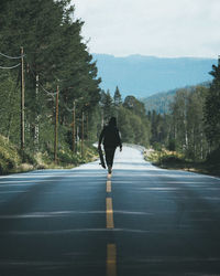 Woman with skateboard walking on road amidst trees