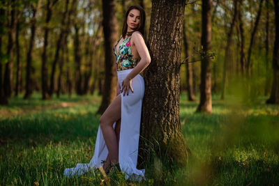 Woman standing by tree trunk in forest