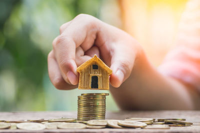 Cropped hand of person balancing model home on stacked coins outdoors