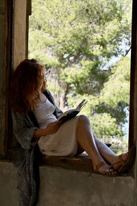 Side view of woman sitting by window
