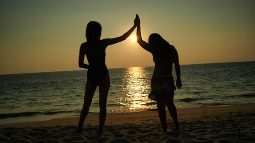 Silhouette woman with arms outstretched at beach during sunset