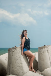 Young woman sitting on beach by sea against sky