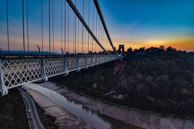 Suspension bridge over river against sky during sunset