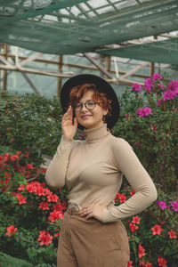 A beautiful plus size girl in eyeglasses and hat smiling among the green plants and flowers.
