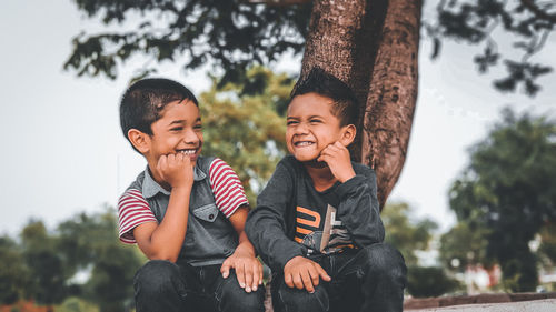 Happy friends sitting against trees