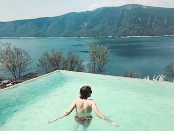 High angle view of man swimming in infinity pool against lake and mountain