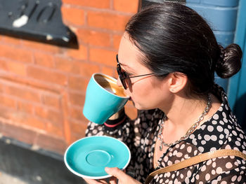 Young candid woman drinking morning coffee in tiffany color ceramic mug with saucer on cafe terrace.