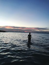 Silhouette man in sea against sky during sunset