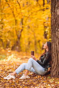 Young woman sitting on tree trunk during autumn