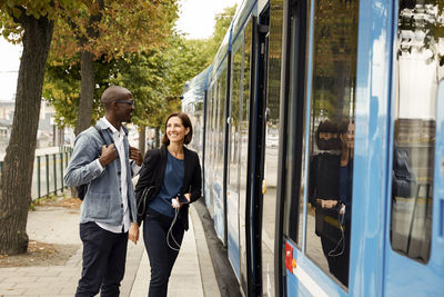 Smiling multi-ethnic commuters standing by blue tram in city