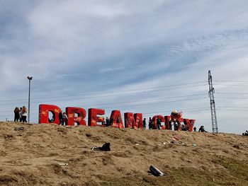 People walking by text on landscape against cloudy sky