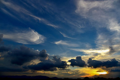 Low angle view of sunlight streaming through clouds during sunset