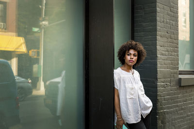 Thoughtful woman looking away while leaning on wall in city