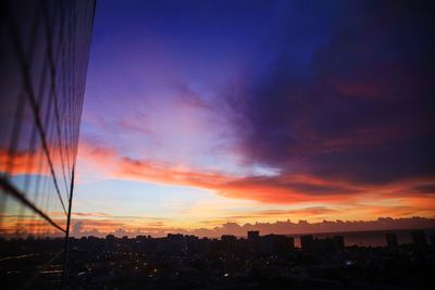 Silhouette buildings against cloudy sky during sunset