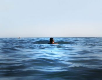 Rear view of person swimming in sea against clear sky