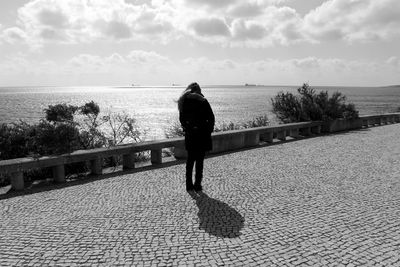 Rear view of woman walking on cobbled walkway by sea against sky